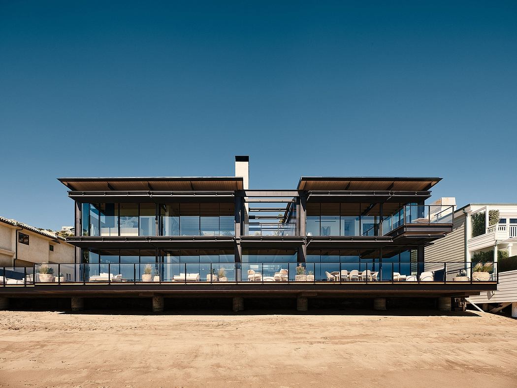 A modern, glass-walled beachfront building with tiered decks and a sleek, wooden roof.