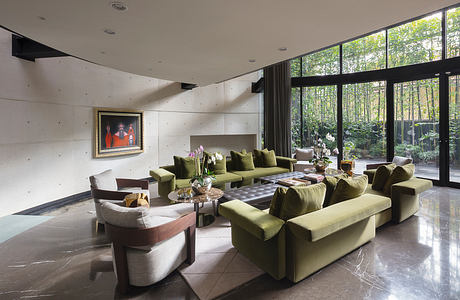 Expansive living room with floor-to-ceiling windows, plush green upholstery, and modern art.