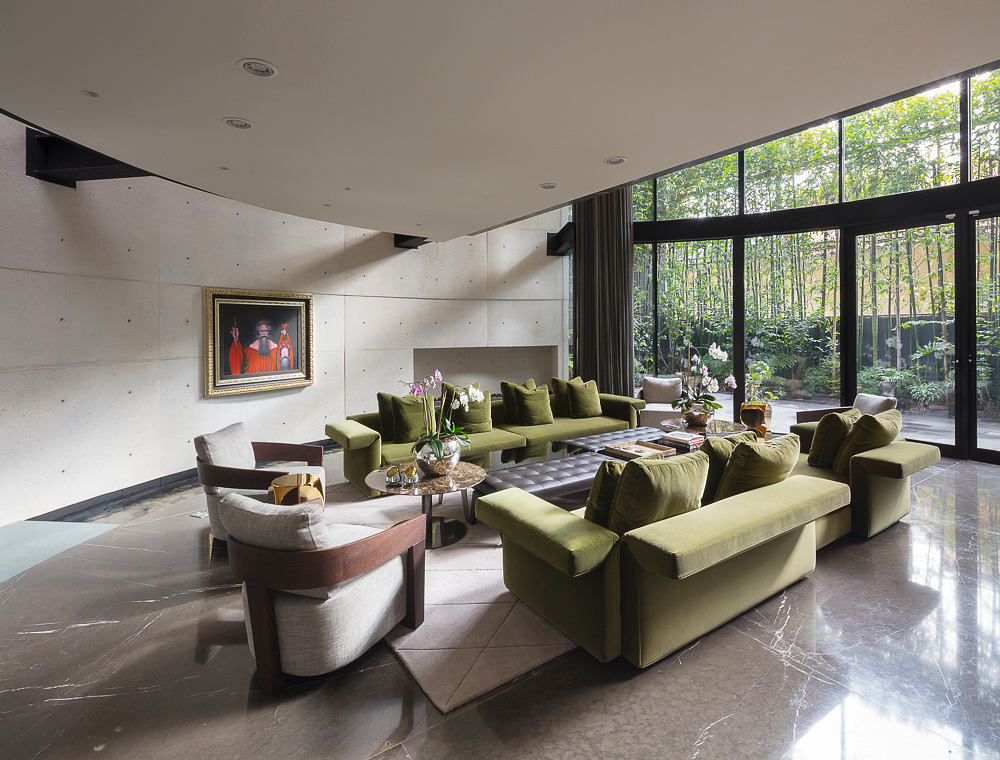 Expansive living room with floor-to-ceiling windows, plush green upholstery, and modern art.