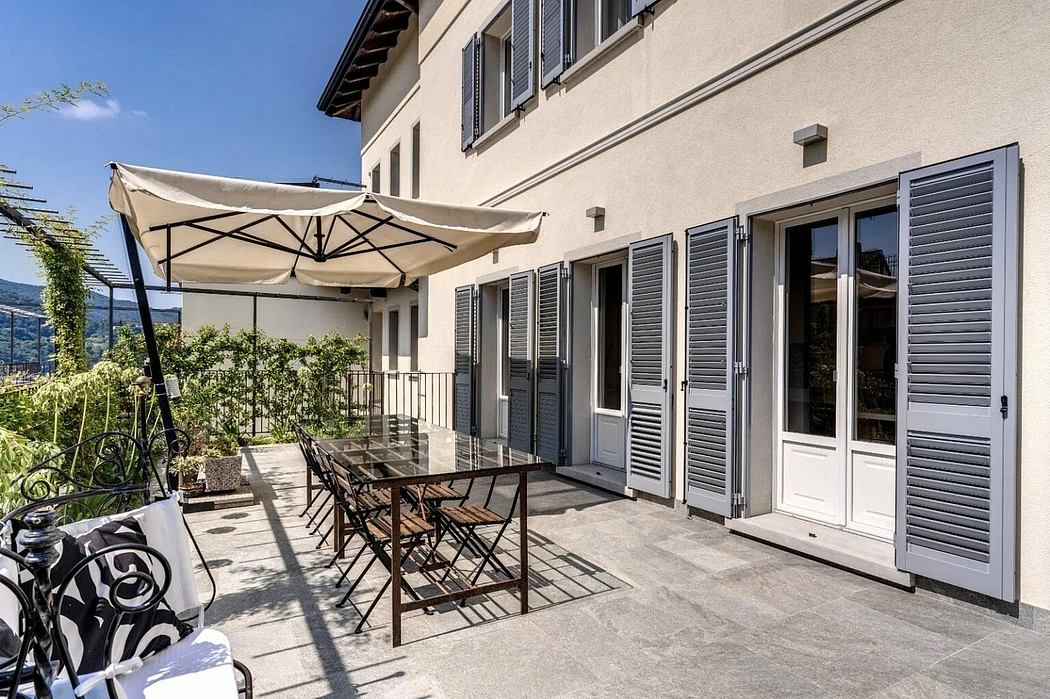 Outdoor patio with umbrella, wooden tables and chairs, and large windows with shutters.