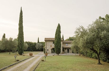 An idyllic Tuscan villa with cypress trees, stone walls, and a grassy courtyard.