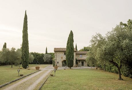 An idyllic Tuscan villa with cypress trees, stone walls, and a grassy courtyard.