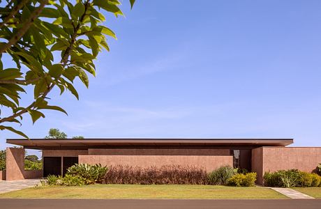 A modern one-story building with a flat roof, wooden beams, and lush landscaping outside.