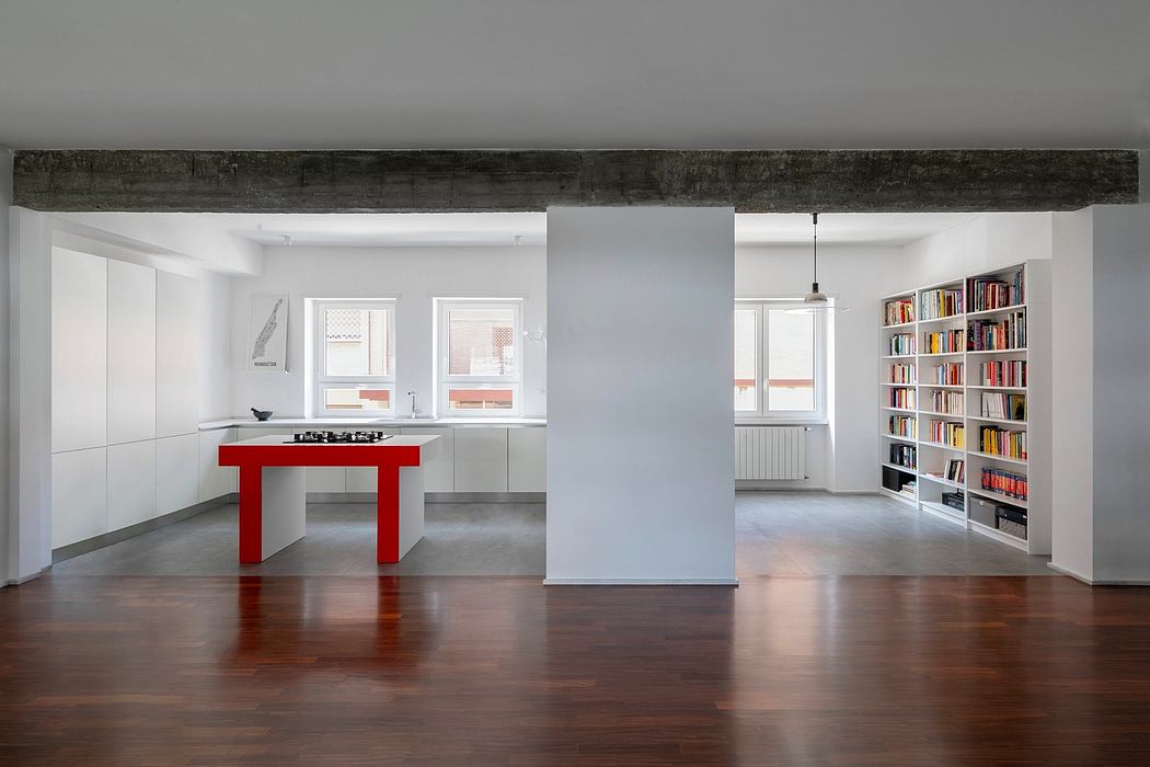 Minimalist kitchen with red dining table, bookshelf wall, exposed wooden beams, and hardwood floors.