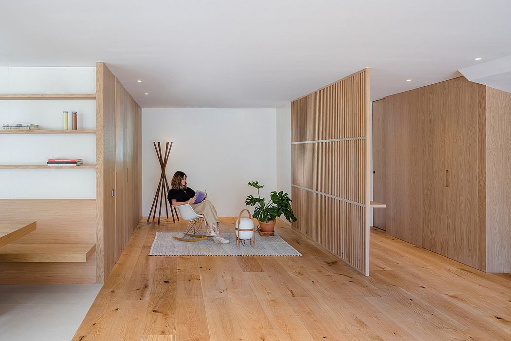 Minimalist living room with wooden accents, built-in storage, and a woman seated on a chair.