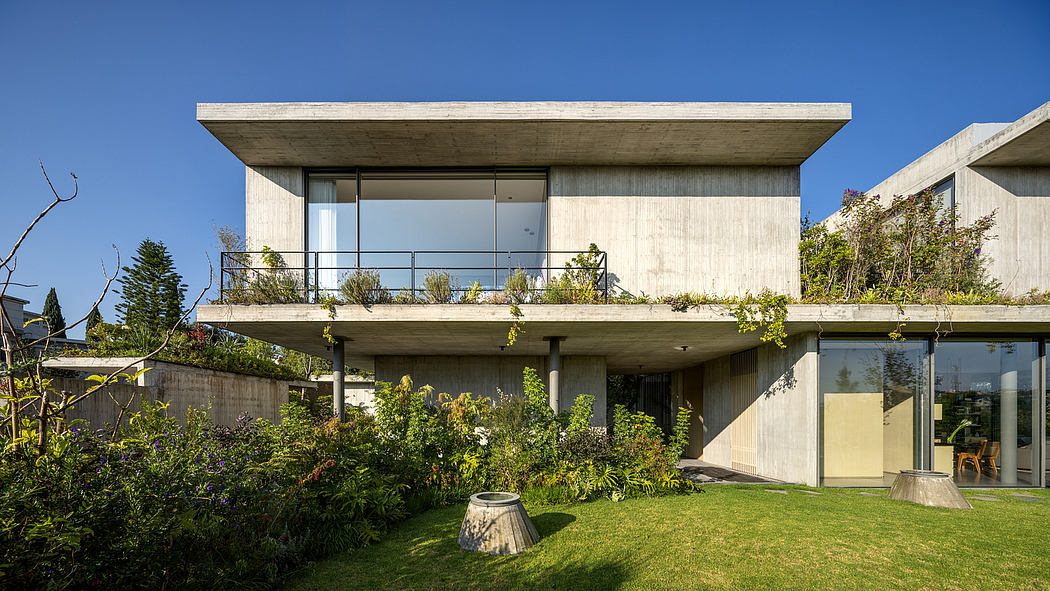 A modern concrete house with a cantilevered upper floor, surrounded by lush greenery.