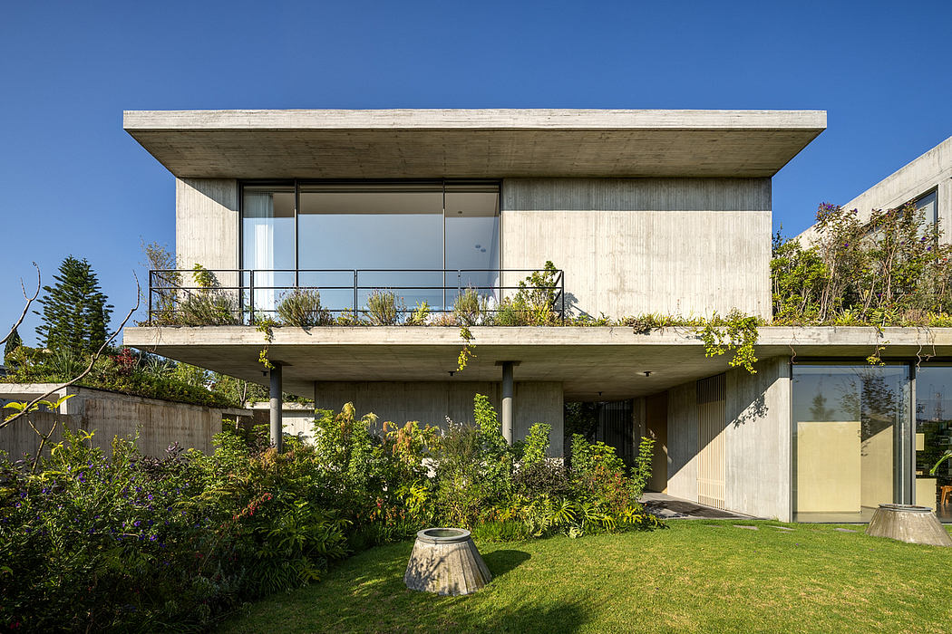 A modern concrete house with a cantilevered upper floor, surrounded by lush greenery.