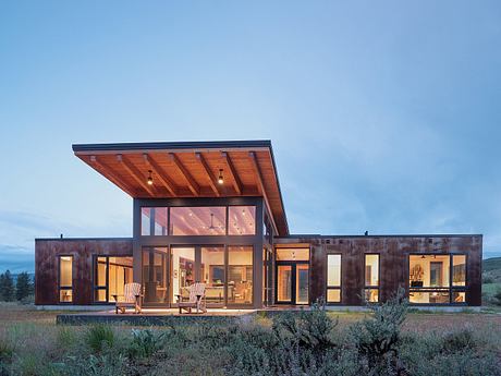 Distinctive wooden-beamed structure with expansive glass walls overlooking a rural landscape.