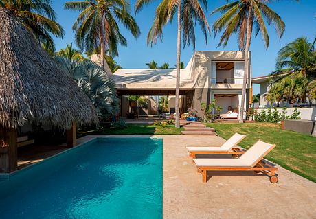 Elegant tropical beach villa with thatched roof, swimming pool, and lush landscaping.