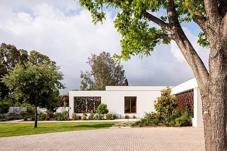 A modern, single-story building with large windows and a brick walkway surrounded by lush vegetation.