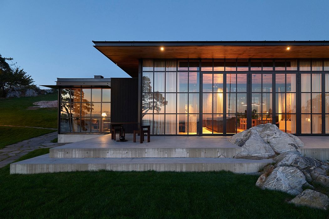 Modern glass and wood structure with a large covered patio and stone accents at dusk.
