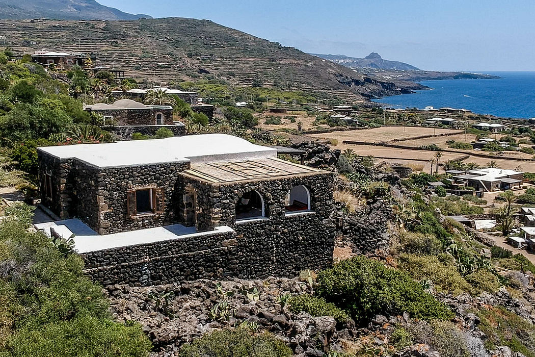 Stone buildings with whitewashed roofs nestled in rugged, lush terrain overlooking the sea.