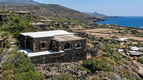 Stone buildings with whitewashed roofs nestled in rugged, lush terrain overlooking the sea.