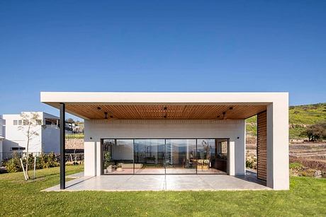 Modern single-story house with wood-paneled ceiling, glass walls, and landscaped yard.