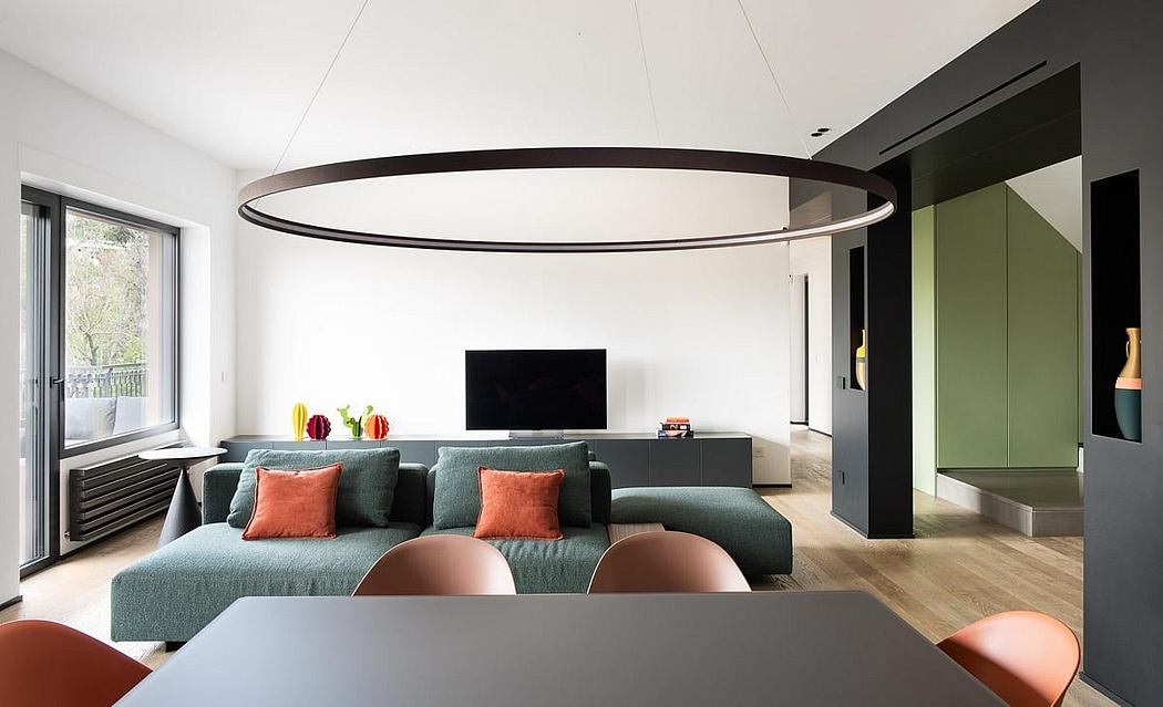 Modern open-plan living space with sleek black lighting fixture, green sofa, wood floors, and TV.
