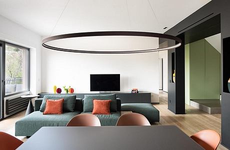 Modern open-plan living space with sleek black lighting fixture, green sofa, wood floors, and TV.