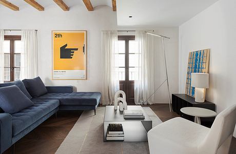 Modern, minimalist living room with wooden beams, white walls, gray sofa, and abstract wall art.