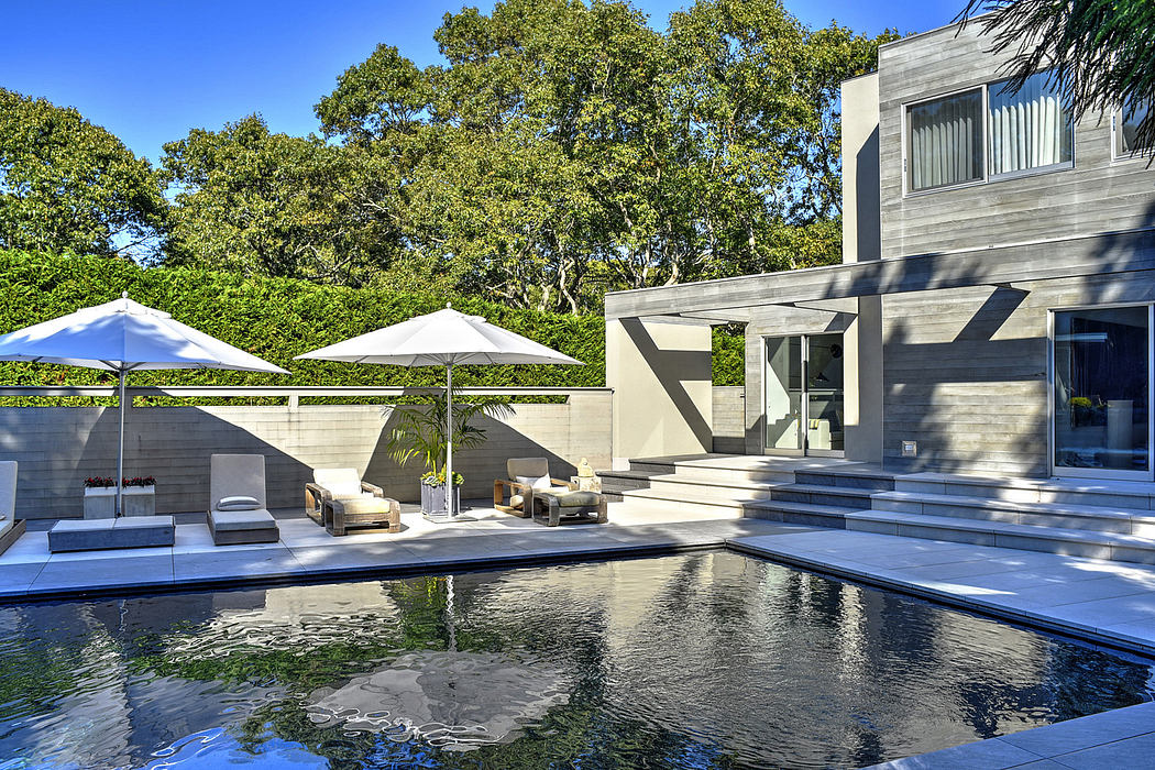 Sleek modern home with a stunning pool surrounded by lush greenery and shady trees.