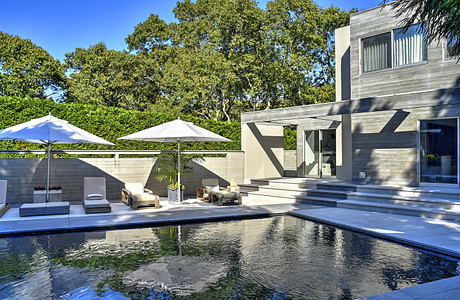 Sleek modern home with a stunning pool surrounded by lush greenery and shady trees.