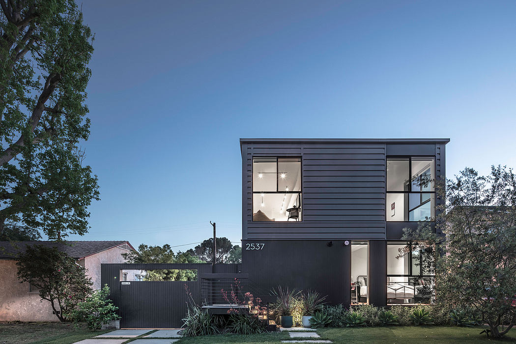 A modern, dark-colored two-story home with large windows, a well-landscaped yard, and a minimalist design.