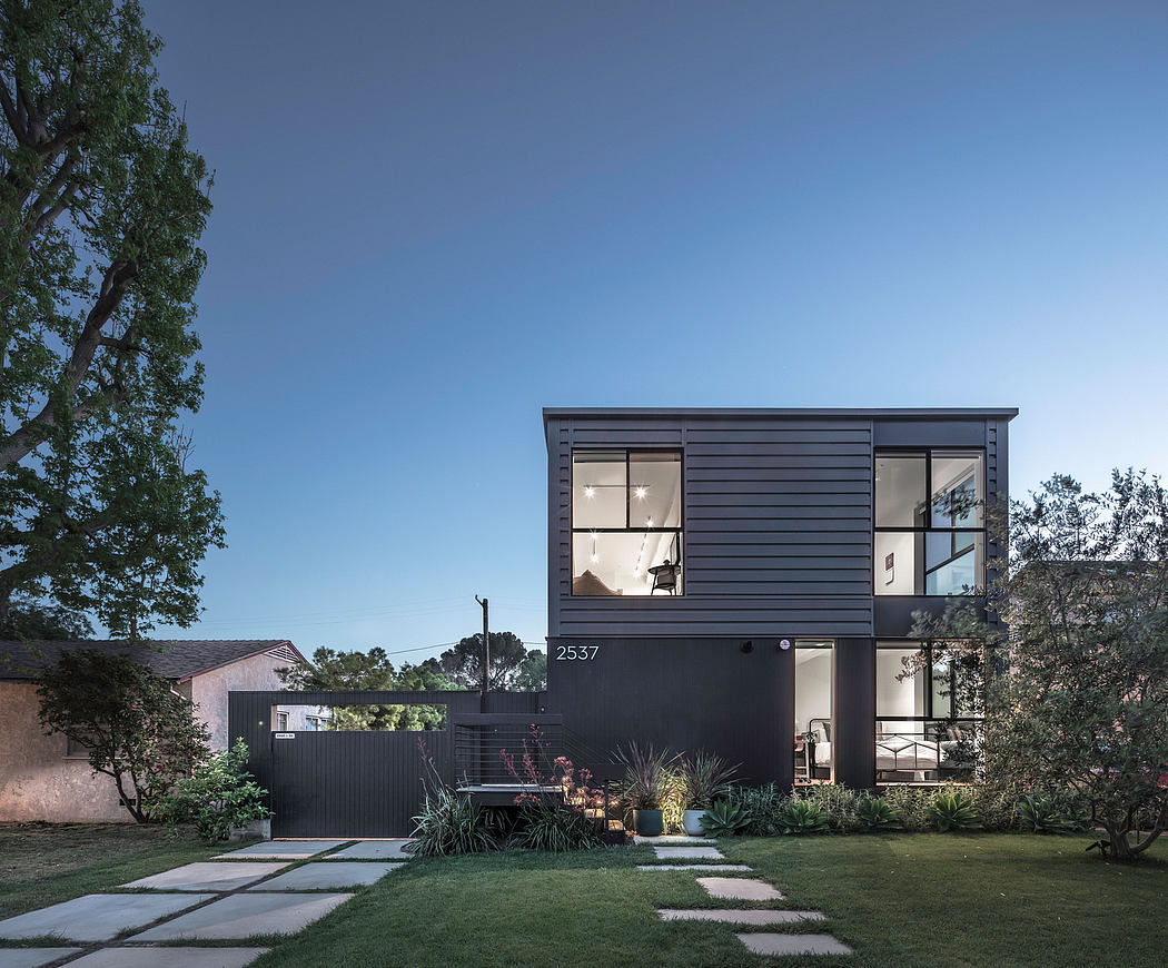 A modern, dark-colored two-story home with large windows, a well-landscaped yard, and a minimalist design.