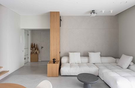 Minimalist living room with a modular white sofa, concrete floor, and wooden accents.