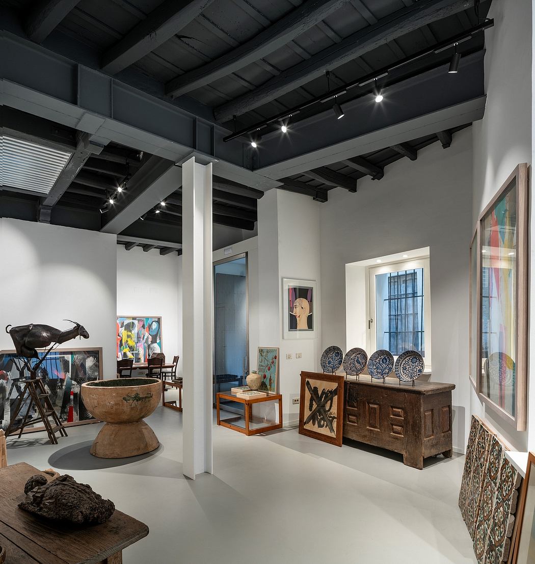 A gallery space with high ceilings, exposed beams, and modern lighting fixtures, showcasing various artworks and decorative items.