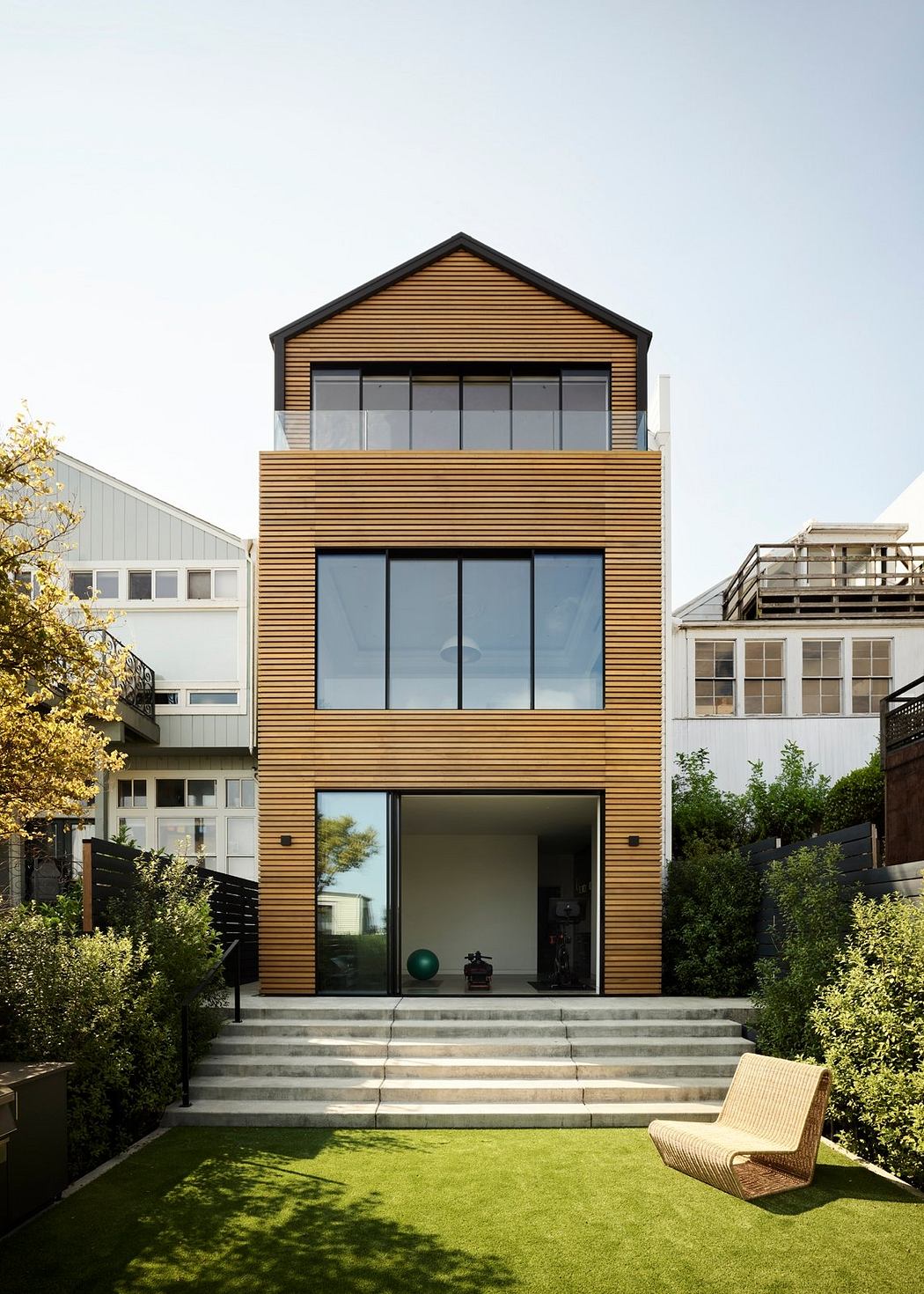 A modern, wood-clad house with large windows, a balcony, and a grassy yard.