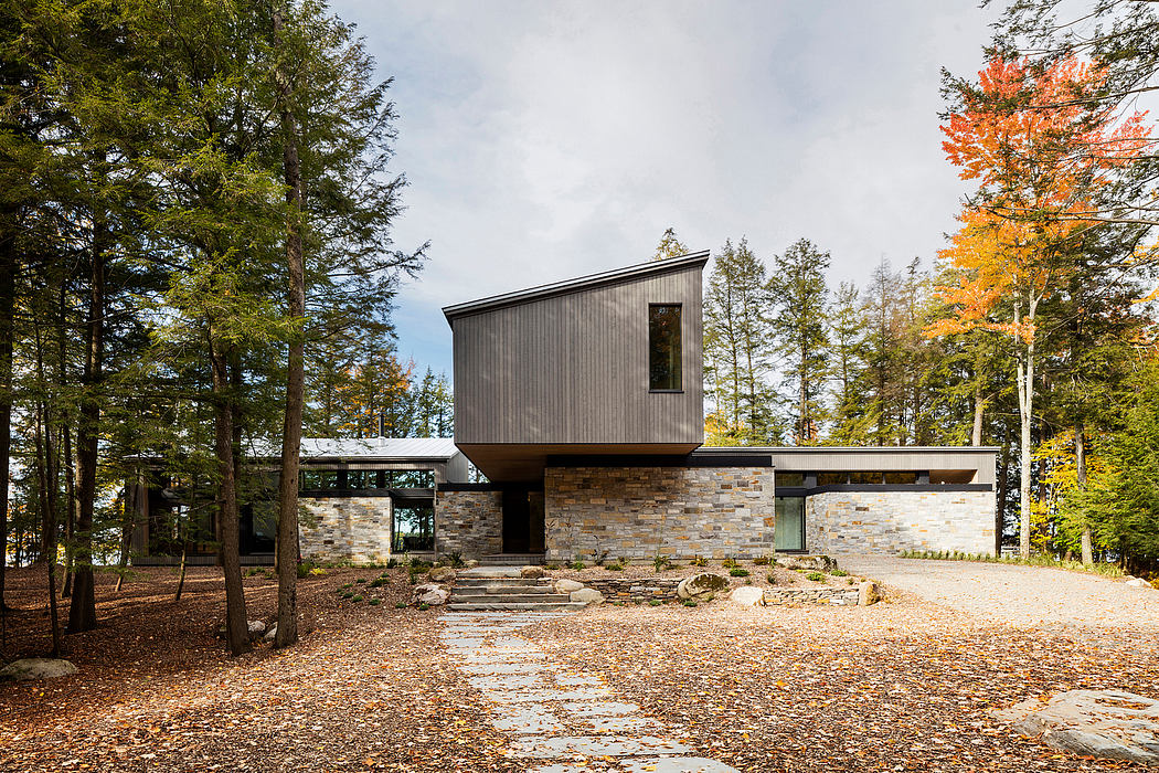 A modern, wooden cabin-style home with large windows and a stone foundation, surrounded by trees.