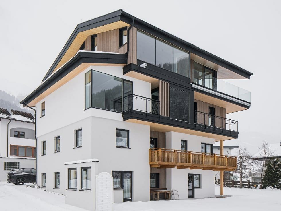 A modern, multi-story building with wooden accents, glass balconies, and a white exterior.
