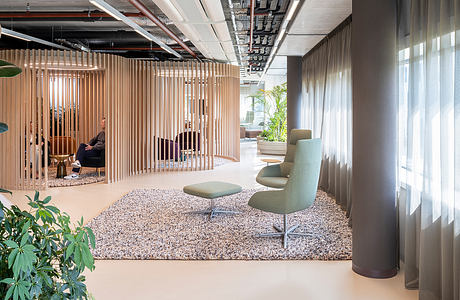 Modern, minimalist office interior with wood slat partitions, cozy furniture, and lush plant life.