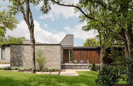 A modern, wood-clad house with a wide porch and large windows nestled among tall trees.