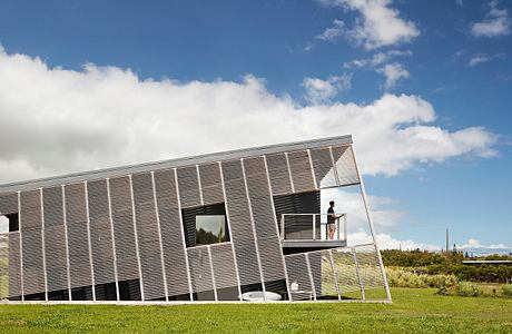 Modern geometric building with a glass façade surrounded by a lush green lawn.