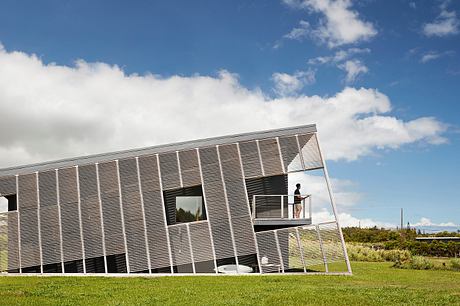 Modern geometric building with a glass façade surrounded by a lush green lawn.