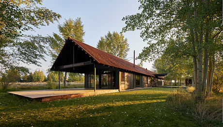 A rustic wooden structure with a sloping roof and covered porch, surrounded by lush greenery.