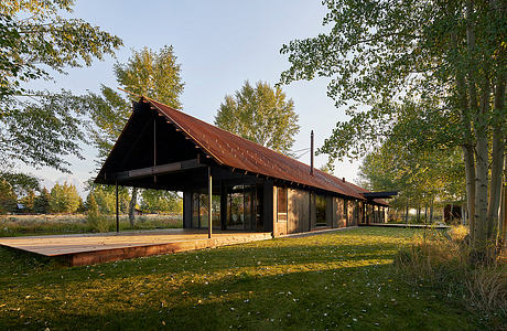 A rustic wooden structure with a sloping roof and covered porch, surrounded by lush greenery.