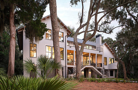 A two-story wooden home with a wide porch and large trees in a lush, tropical setting.