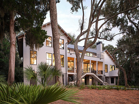 A two-story wooden home with a wide porch and large trees in a lush, tropical setting.