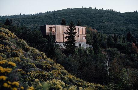 A modern, wooden cabin-style structure nestled among lush, forested hills.