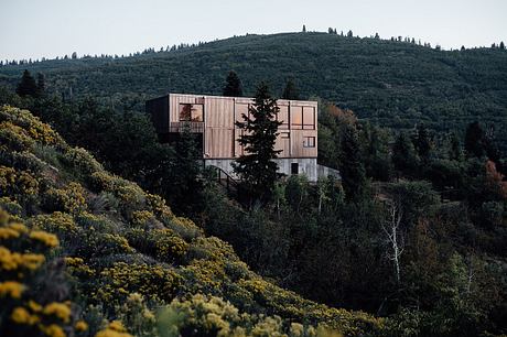 A modern, wooden cabin-style structure nestled among lush, forested hills.