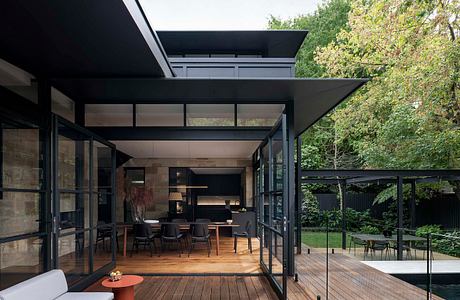 A striking modern pavilion with expansive glass walls, wood decking, and lush greenery.