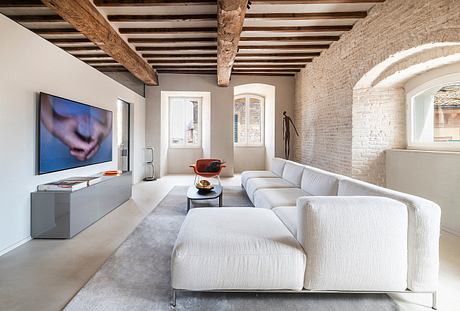 Spacious living room with exposed wooden beams, brick walls, and a large modern TV.