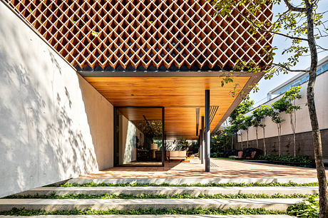 A modern outdoor patio with a geometric wooden roof structure, surrounded by lush greenery.