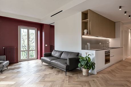 Minimalist open-concept living space with burgundy accent wall, grey sofa, and modern kitchen.