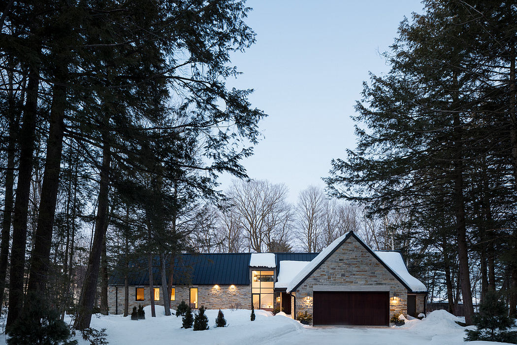 Modern country home with stone facade, gable roof, and warm lighting in snowy landscape.