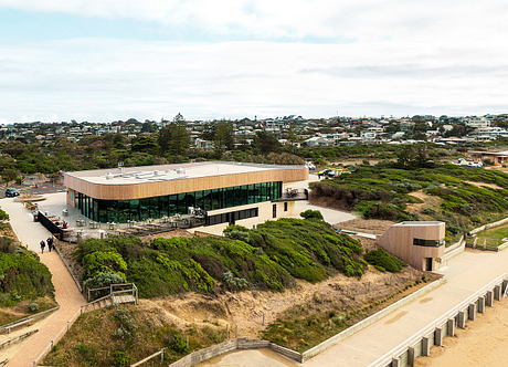 Modern building with wooden exterior situated on a hillside overlooking a coastal town.