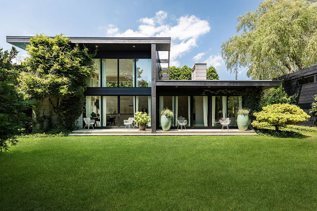 Modern glass-walled home with lush green lawn, covered patio, and large ceramic planters.
