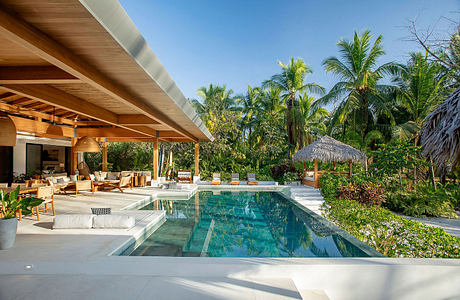 Luxurious tropical villa with thatched roof, infinity pool, and lush vegetation.