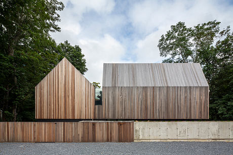 Modernist building with wooden siding and simple geometric forms nestled among trees.