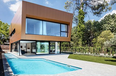 Modern architectural design featuring floor-to-ceiling glass, sleek copper panels, and a swimming pool surrounded by lush greenery.